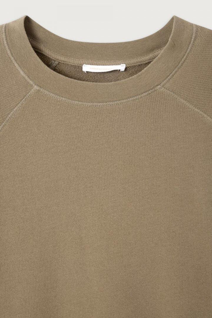 Close-up of a beige sweatshirt with a visible brand label on a light gray background