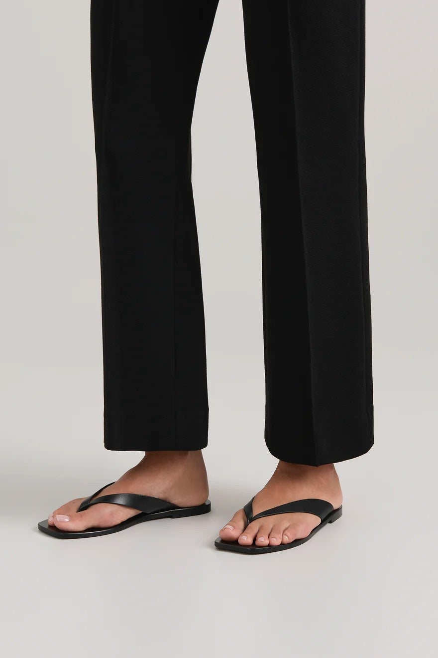 Person wearing black sandals and black pants on a light gray background