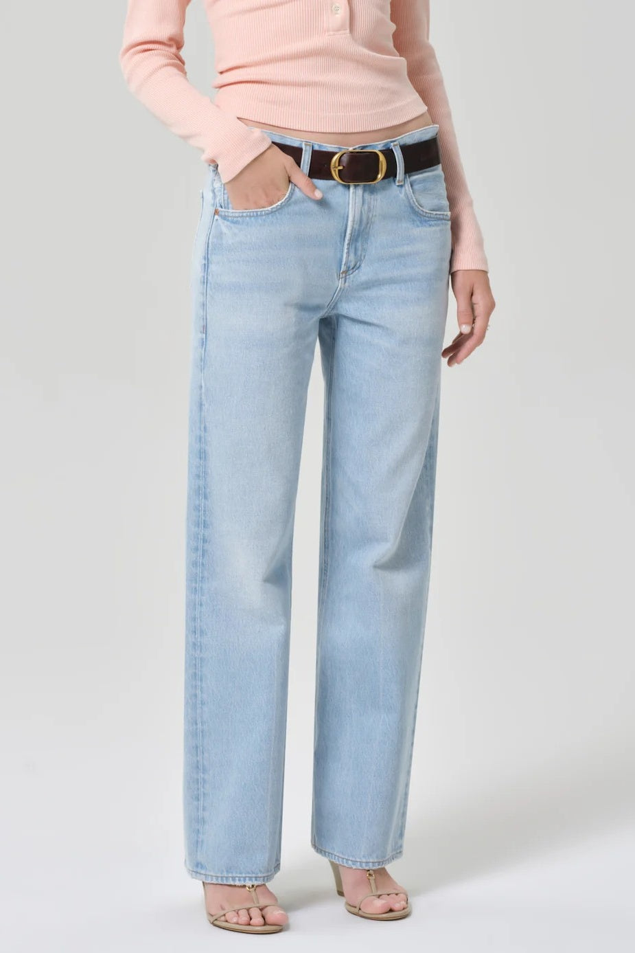 Person wearing light blue jeans and a pink top on a plain background