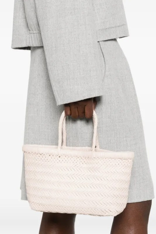 Person holding a woven beige handbag with a plain background