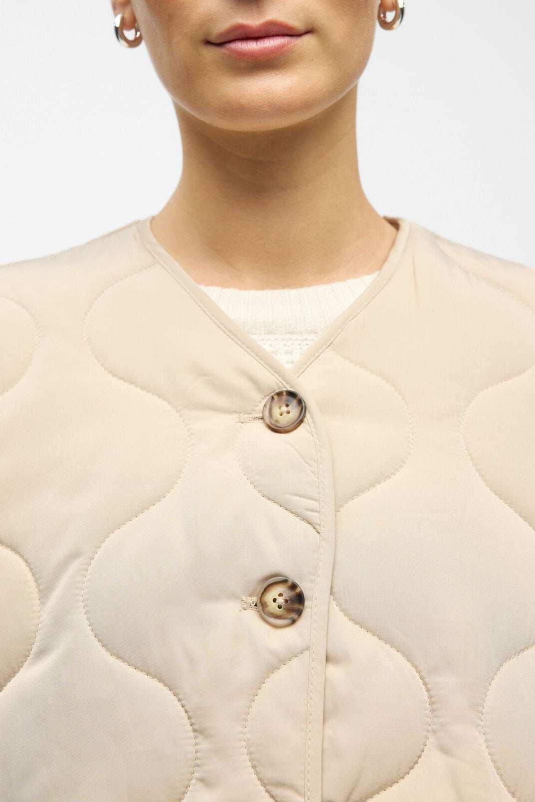 Close-up of a beige quilted jacket with button details on a neutral background
