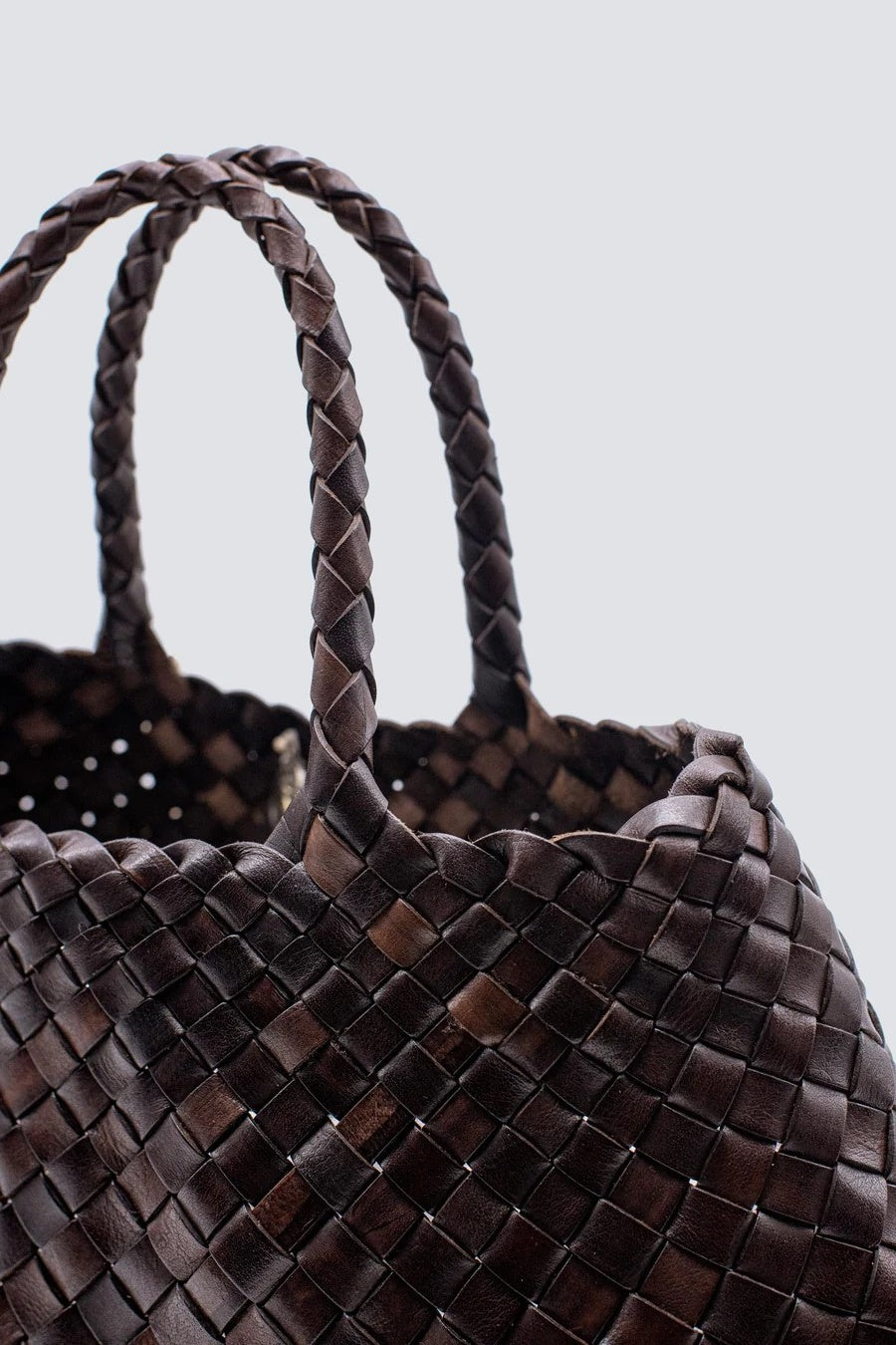 Close-up of a braided brown leather handbag on a light gray background