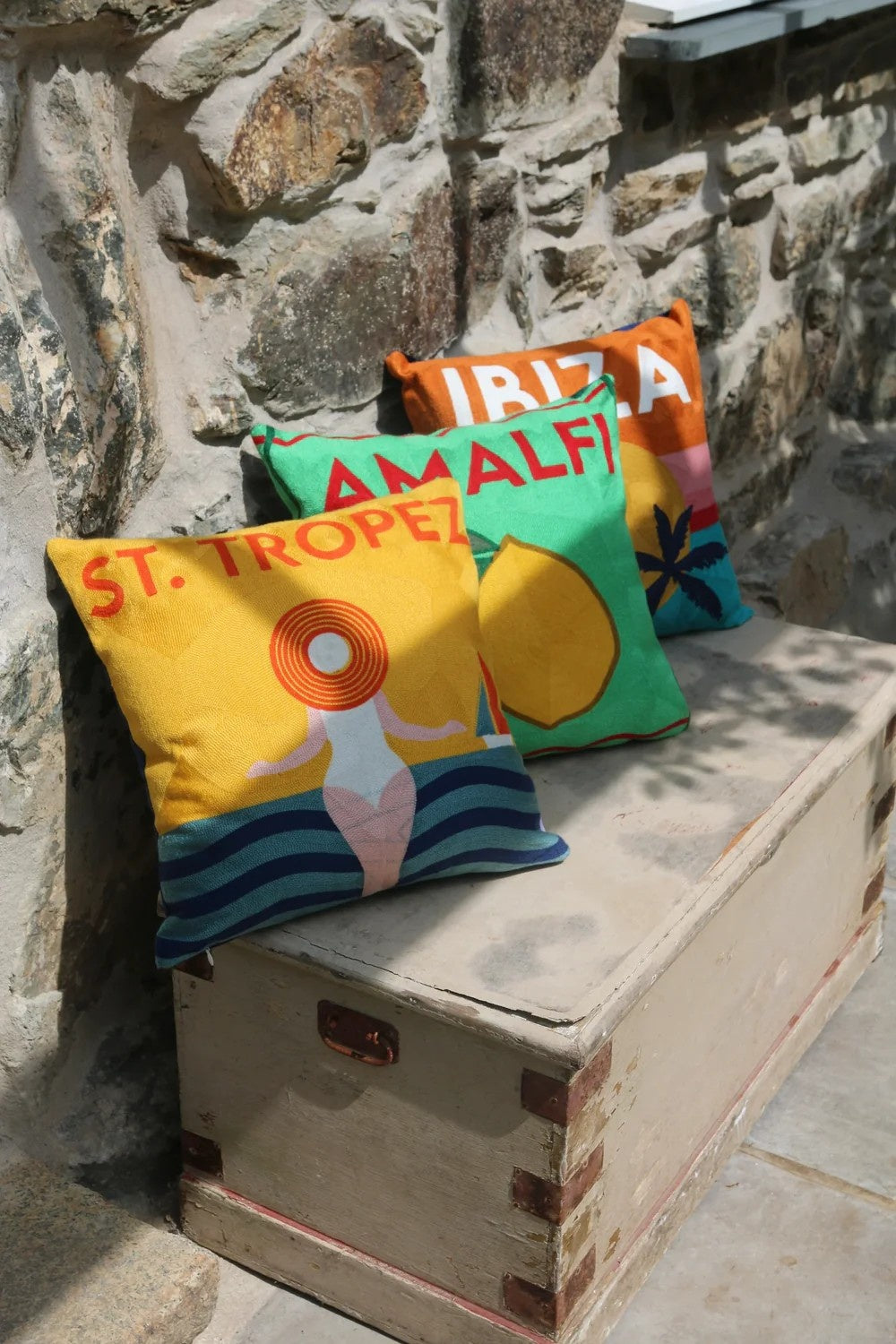 Colorful pillows with text and graphics on a stone bench.