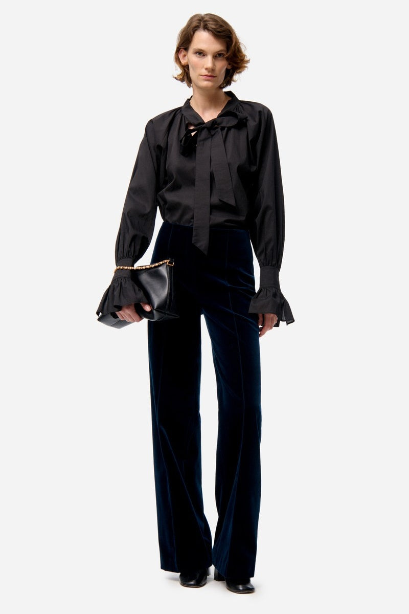 Woman wearing a black blouse and pants holding a black clutch on a white background