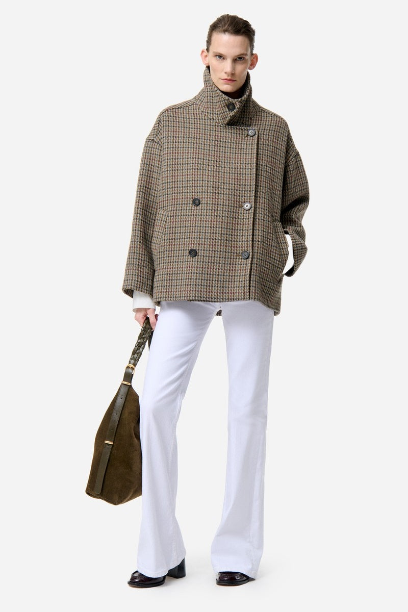 Model wearing a Vanessa Bruno plaid coat and white trousers holding a brown bag on a white background