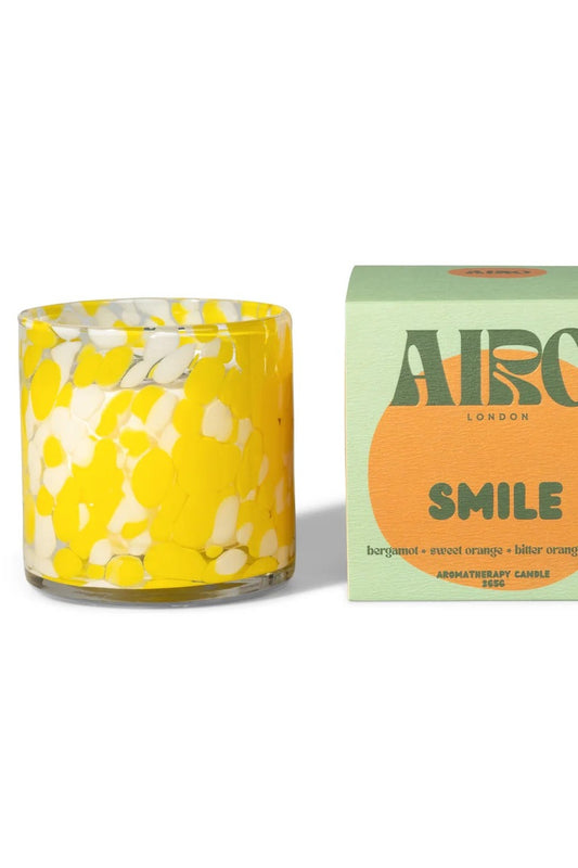 Yellow floral candle in a glass holder with a green box labeled 'Airo London Smile' on a white background.