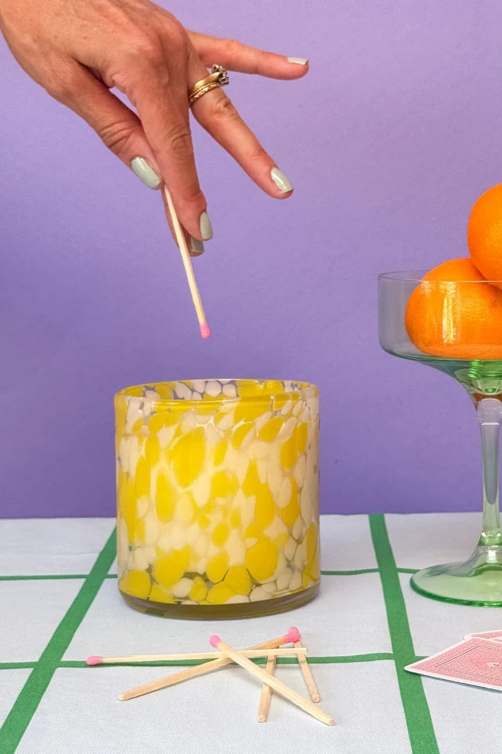 Hand lighting a yellow candle with a purple background
