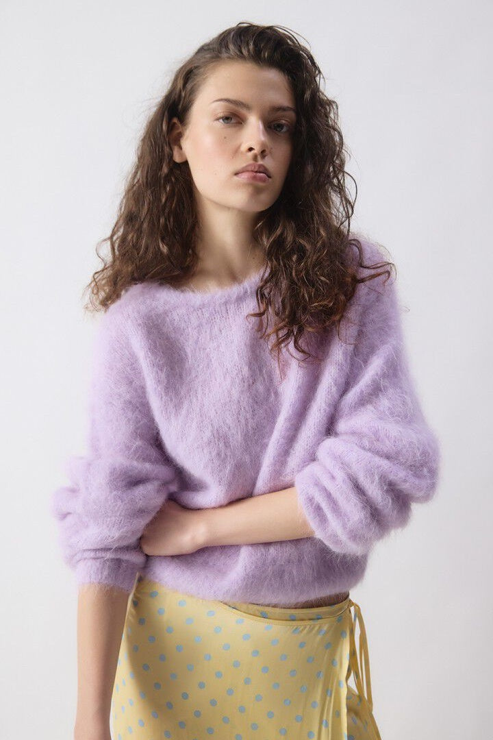 Woman wearing a light purple sweater and yellow skirt with a white background