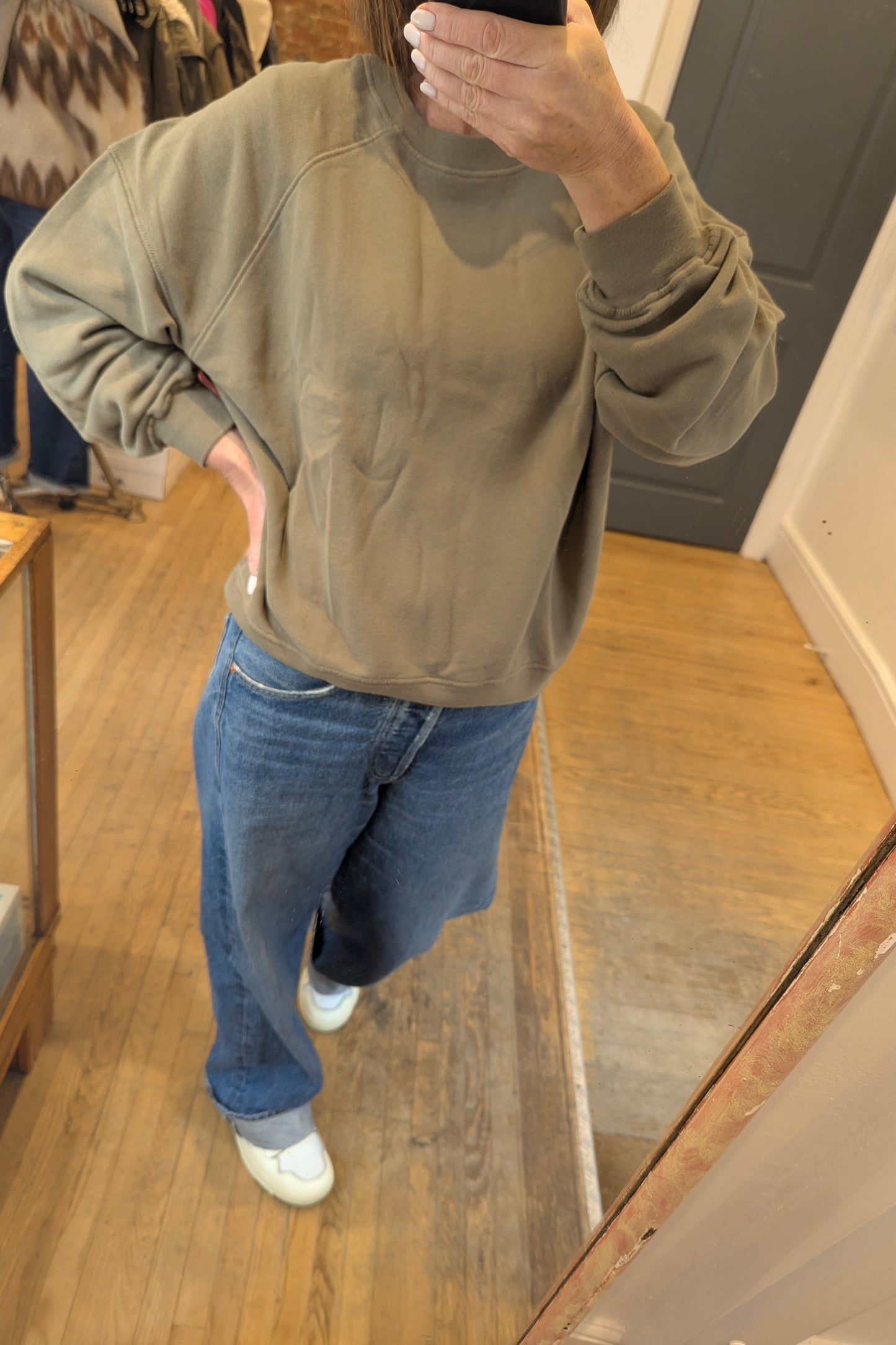 Person wearing a beige american vintage sweatshirt and blue jeans standing in front of a mirror.