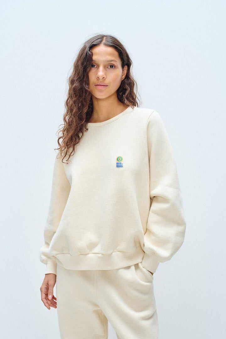 Woman wearing a cream-colored sweatshirt with a small logo on a light grey background