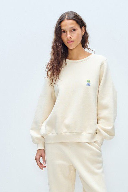 Woman wearing a cream-colored sweatshirt with a logo on a white background