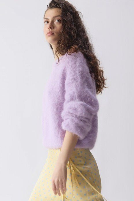Woman wearing a light purple sweater and yellow skirt against a white background