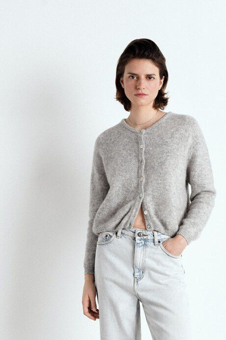 Person wearing a grey cardigan and light blue jeans on a white background