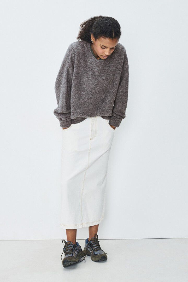 Person wearing a grey sweater and white pants against a white background