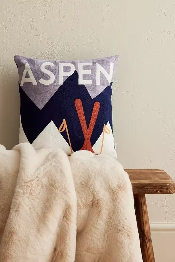 Decorative pillow with 'ASPEN' text on a chair with a blanket