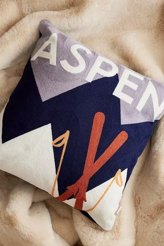 Decorative pillow with 'ASPEN' text and ski design on a beige blanket