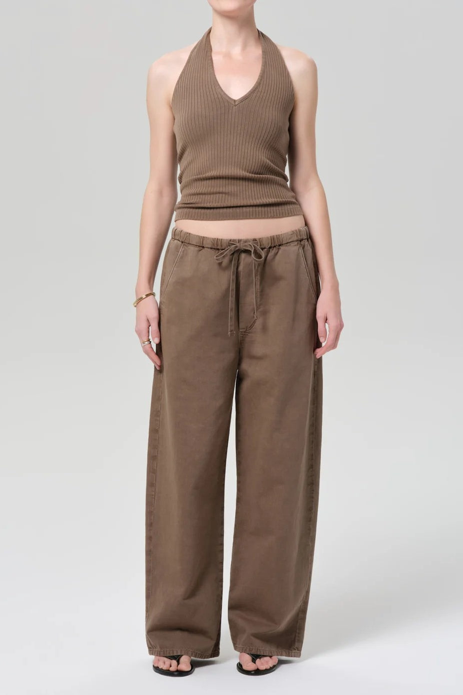 A model wearing a brown ribbed halter crop top and matching wide-leg drawstring pants, photographed against a light gray studio background.