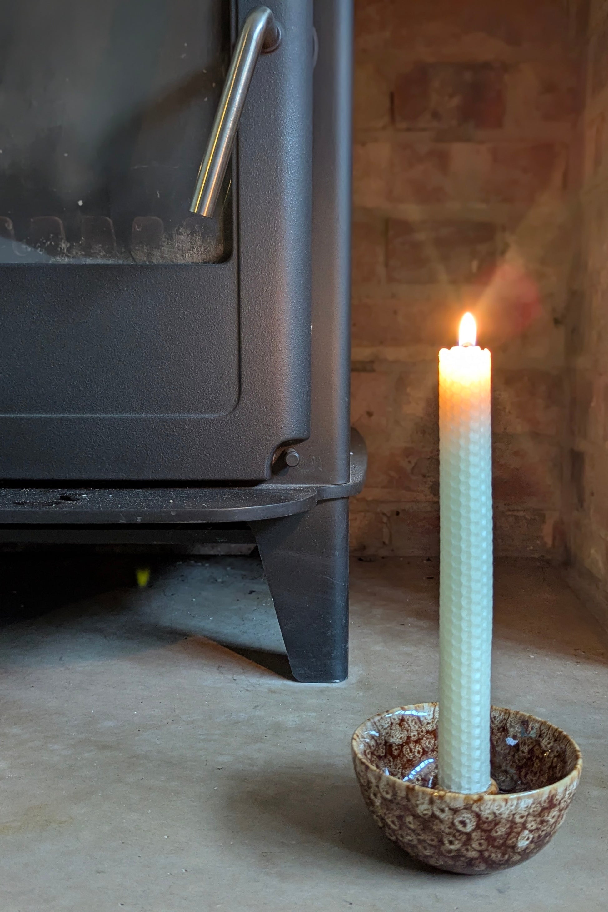 Candle in a decorative holder in front of a wood stove.