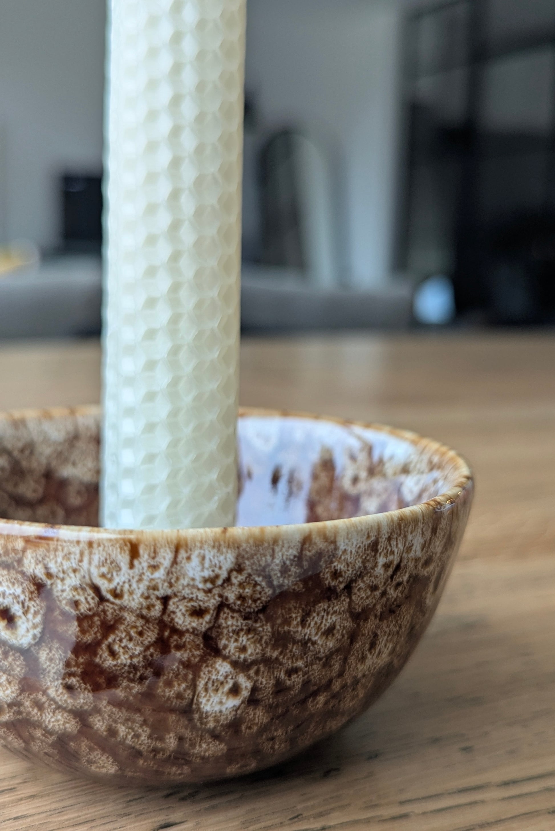 Ceramic bowl with textured white candle inside on a wooden surface