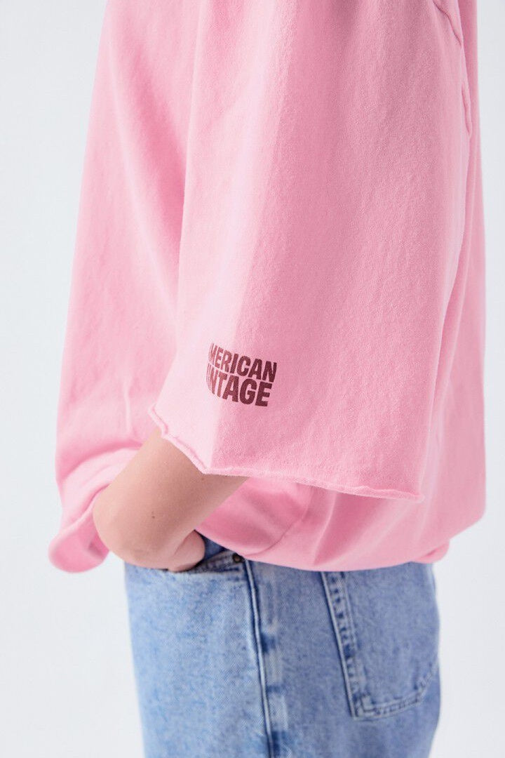 Pink sweatshirt with 'American Vintage' logo worn by a person on a white background