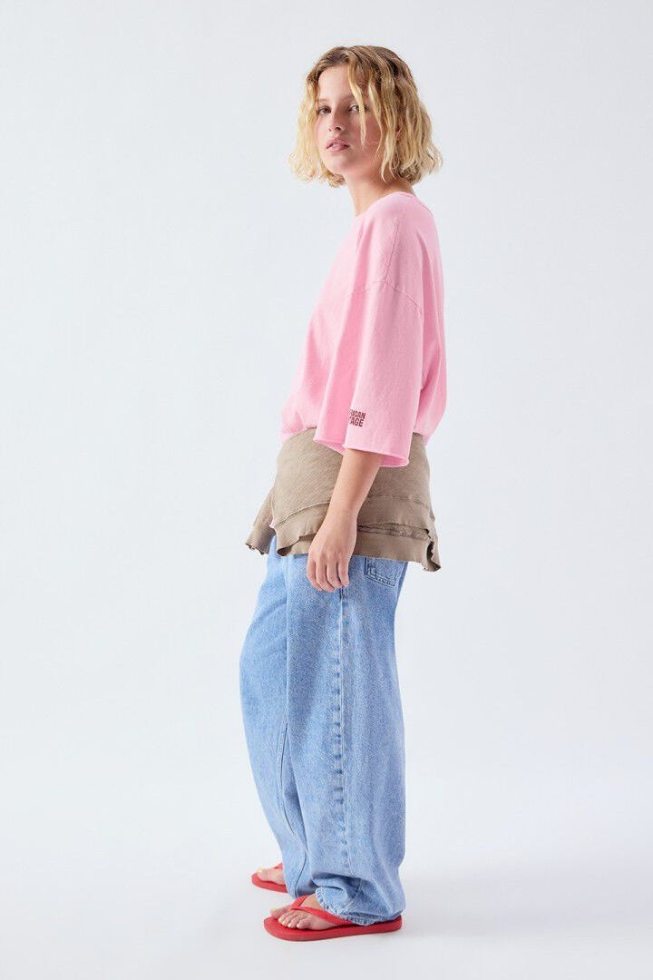 Person wearing a pink tshirt, beige jacket, and blue pants on a white background