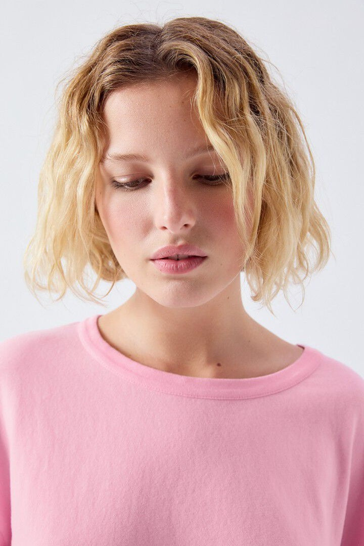 Woman with short blonde hair wearing a pink shirt against a white background