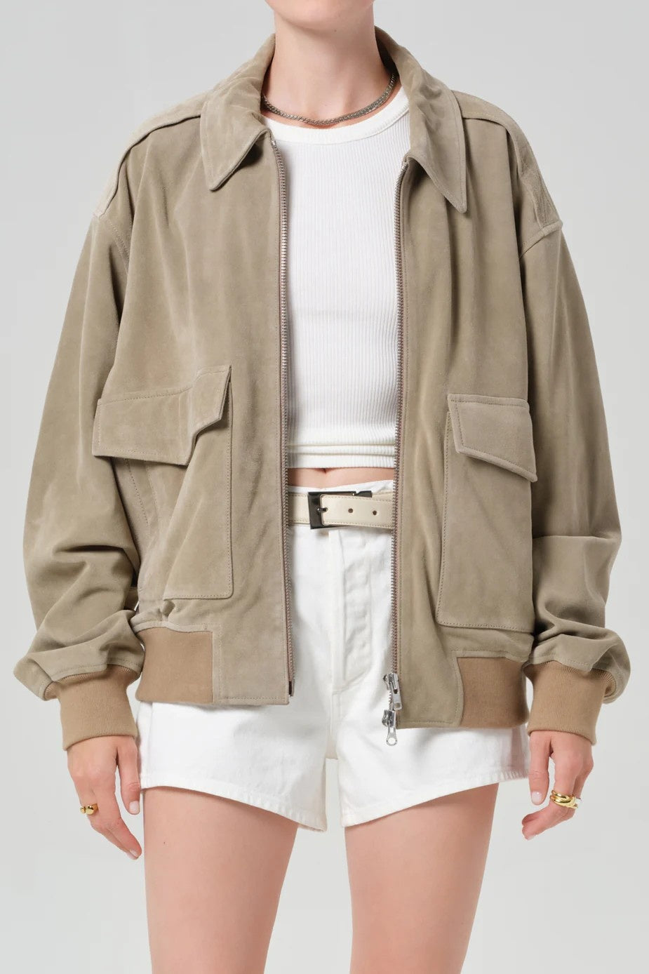 Person wearing a beige jacket over a white top and shorts on a plain background