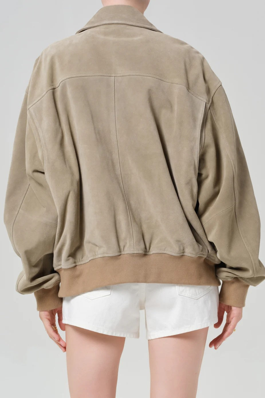 Person wearing a beige jacket and white shorts on a plain background