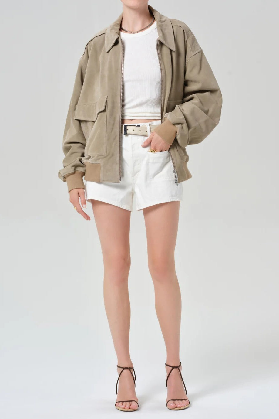 Person wearing a beige jacket, white shirt, and shorts on a plain background