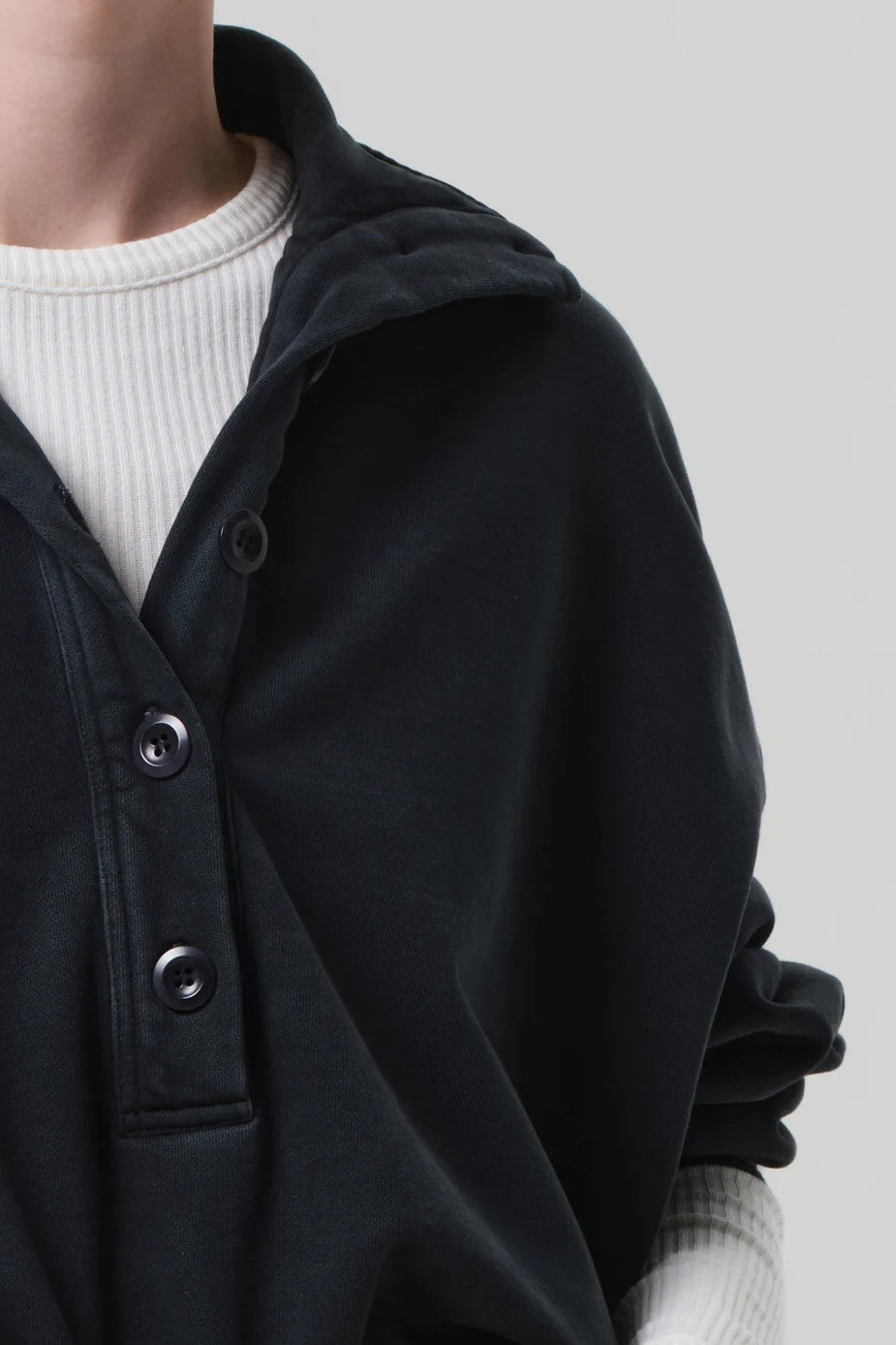 Black jacket with button details worn over a white sweater on a neutral background