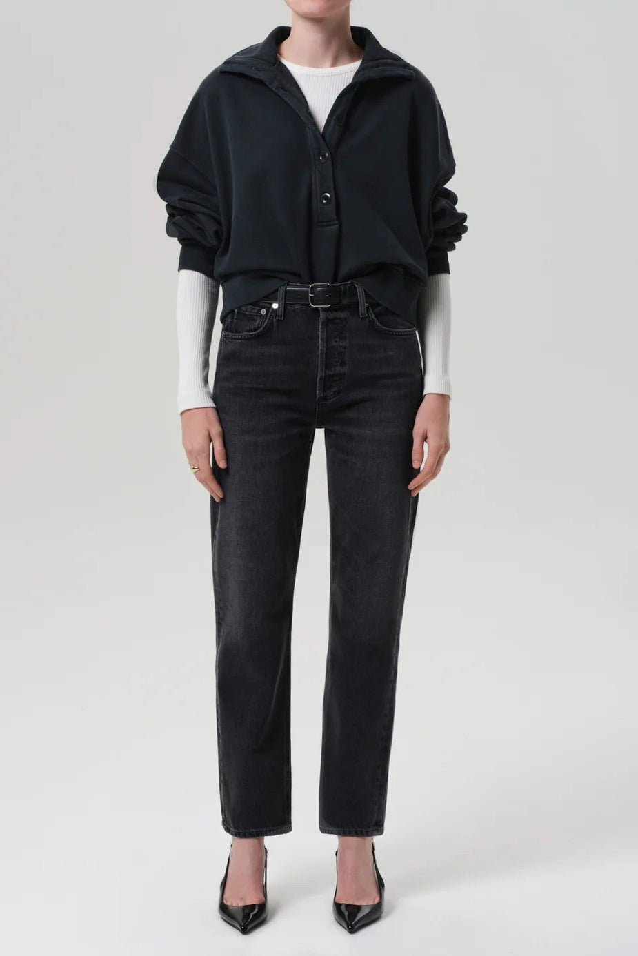 Person wearing a black outfit with a white shirt underneath on a plain background