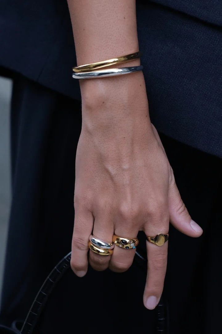 Hand wearing gold rings and bracelets against a dark background