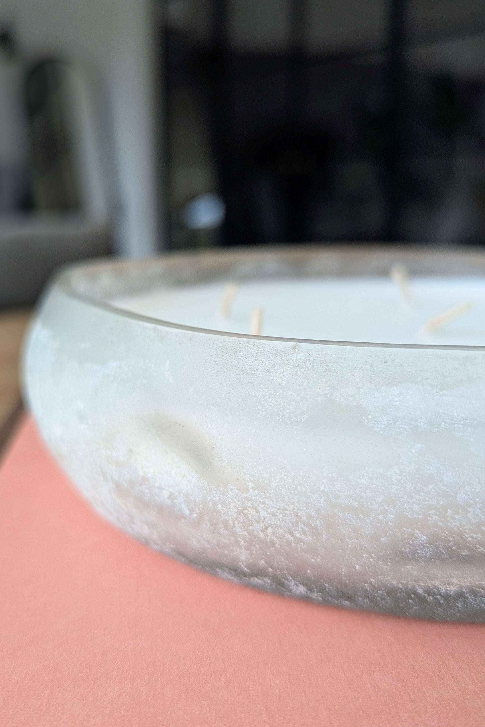 Close-up of a candle with wicks in a glass container on a pink surface.