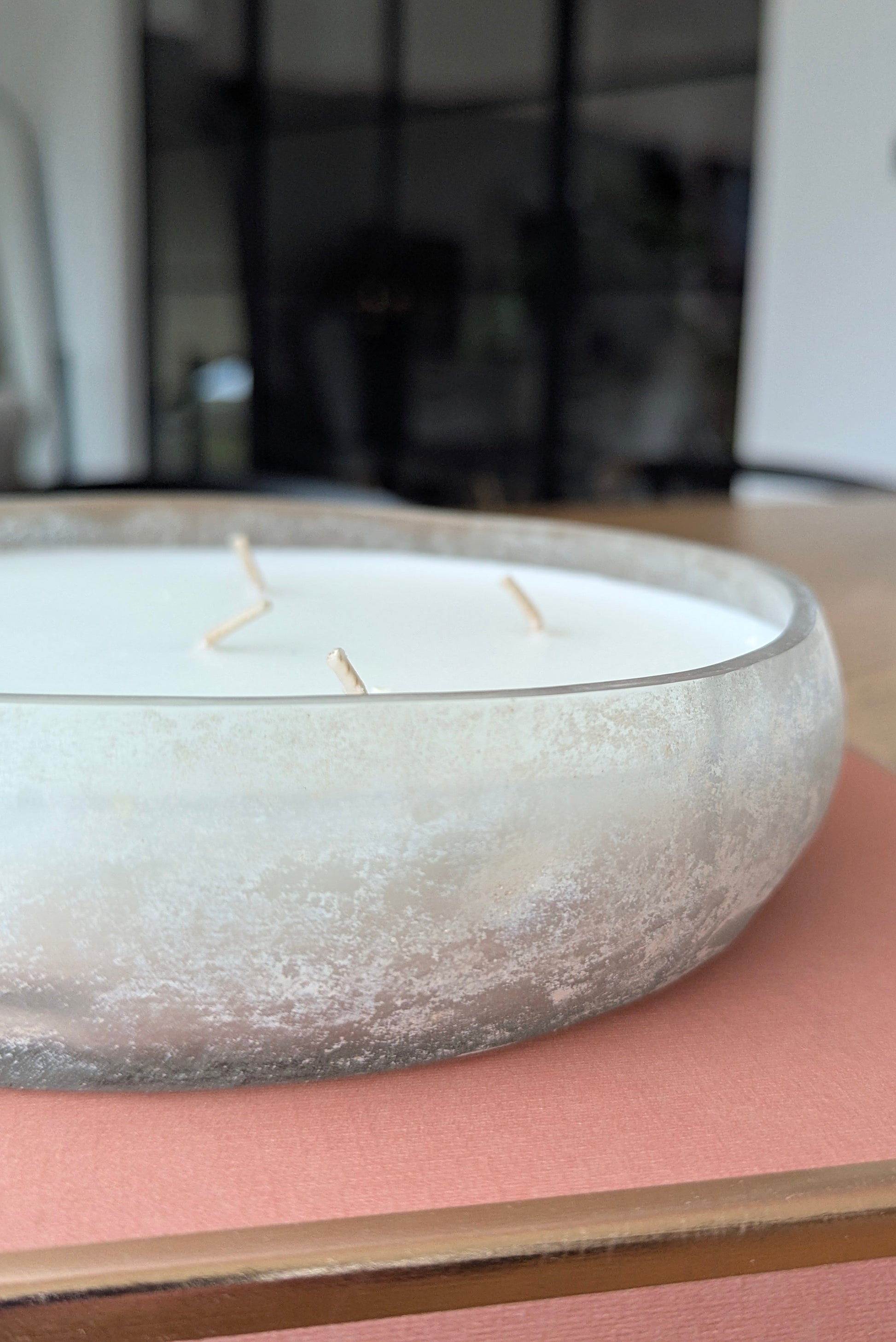 Candle in a glass holder on a pink surface with a blurred background
