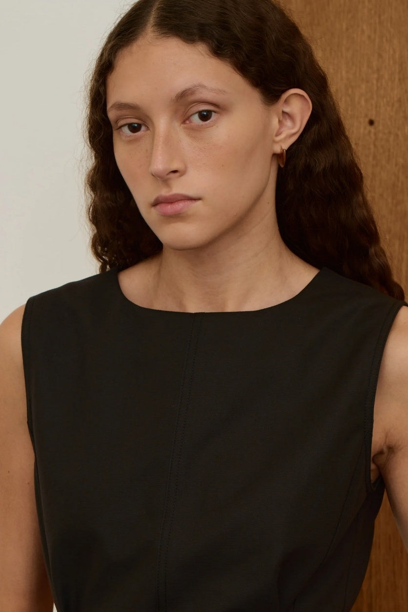 Woman wearing a black sleeveless top and gold earrings against a neutral background