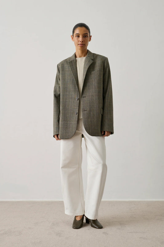 Person wearing a beige checkered blazer and white pants on a plain background