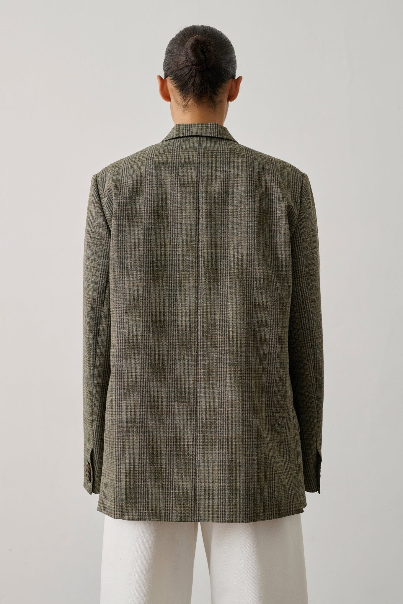Person wearing a beige checkered jacket on a plain background