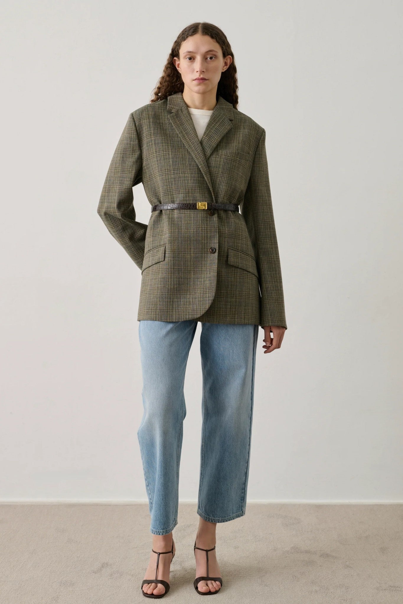 Woman wearing a beige plaid blazer and light blue jeans against a white background