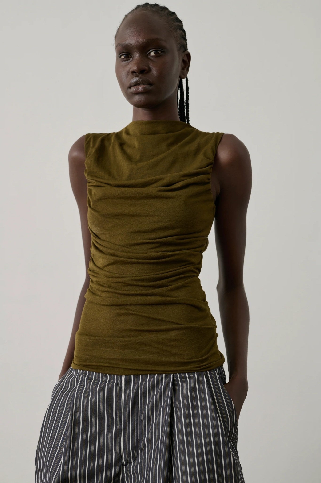 Woman wearing a broze sleeveless top and striped pants against a plain background