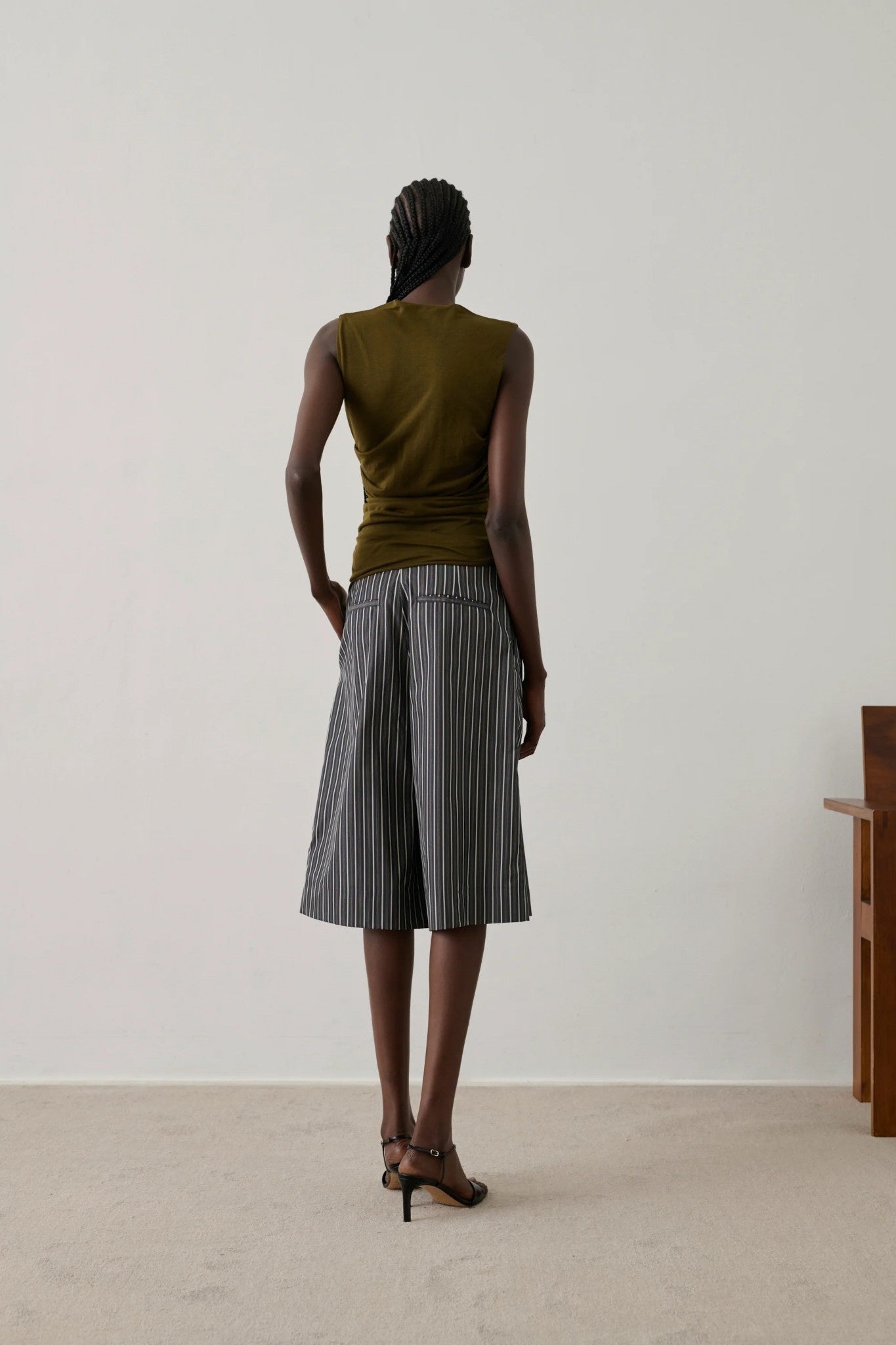 Person wearing a sleeveless top and striped pants standing against a plain white wall.