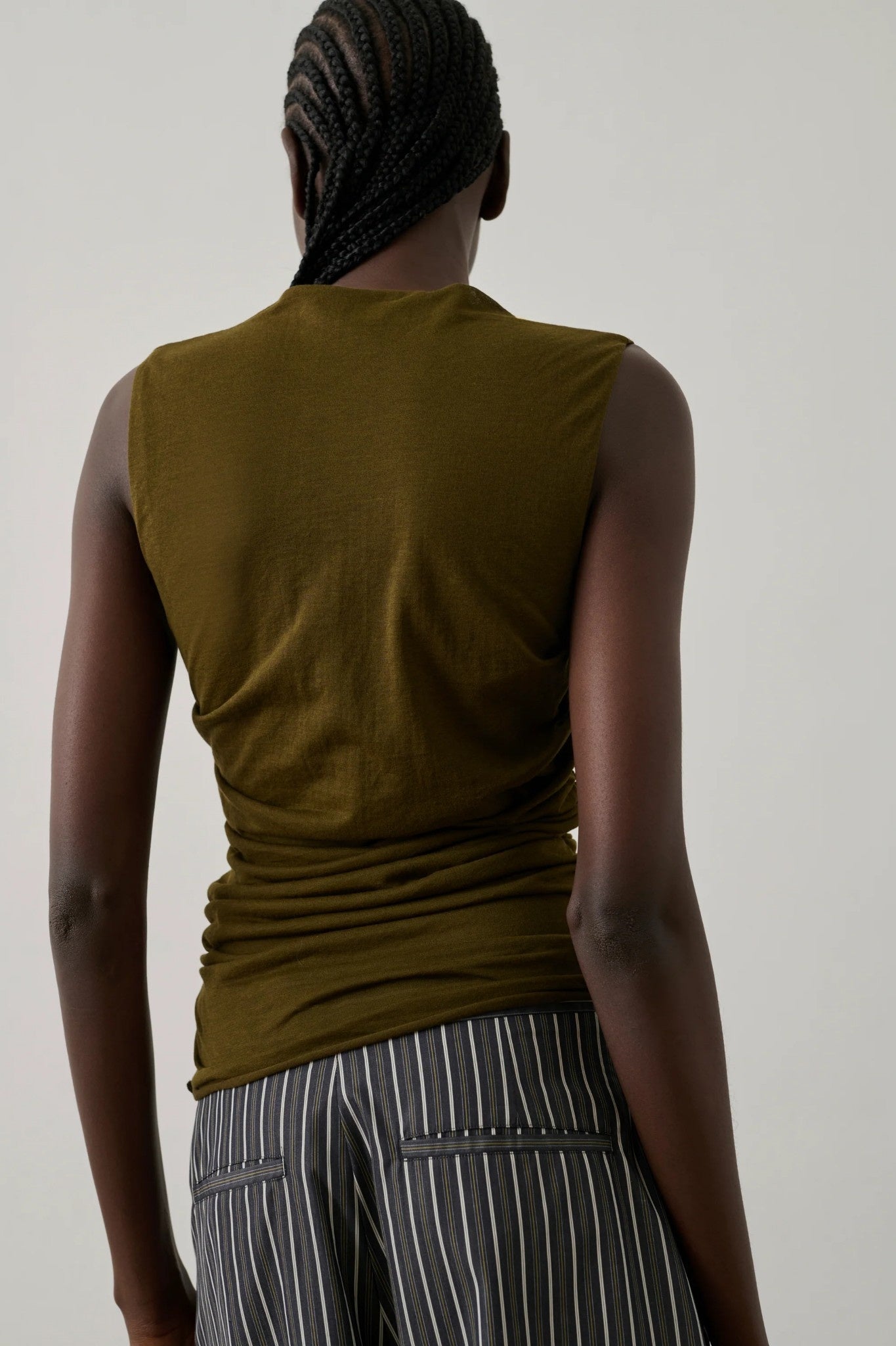 Person wearing a sleeveless bronze top and striped pants against a plain background