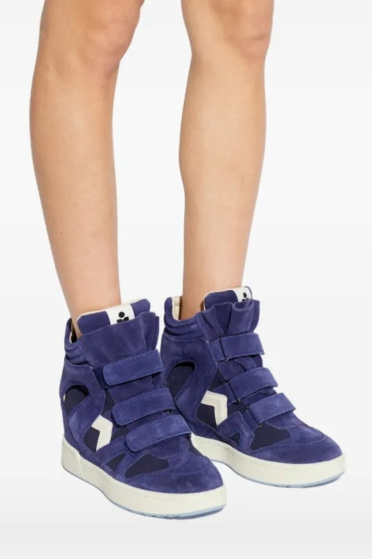 Blue high-top sneakers with white soles worn by a person on a light gray background