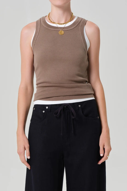 Person wearing a brown sleeveless top and black pants on a gray background