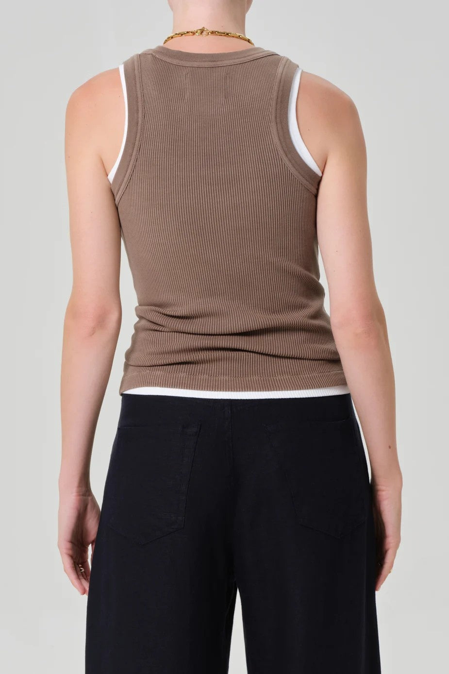 Rust brown ribbed tank top shown from the back on a model, paired with black wide-leg trousers against a light gray background.