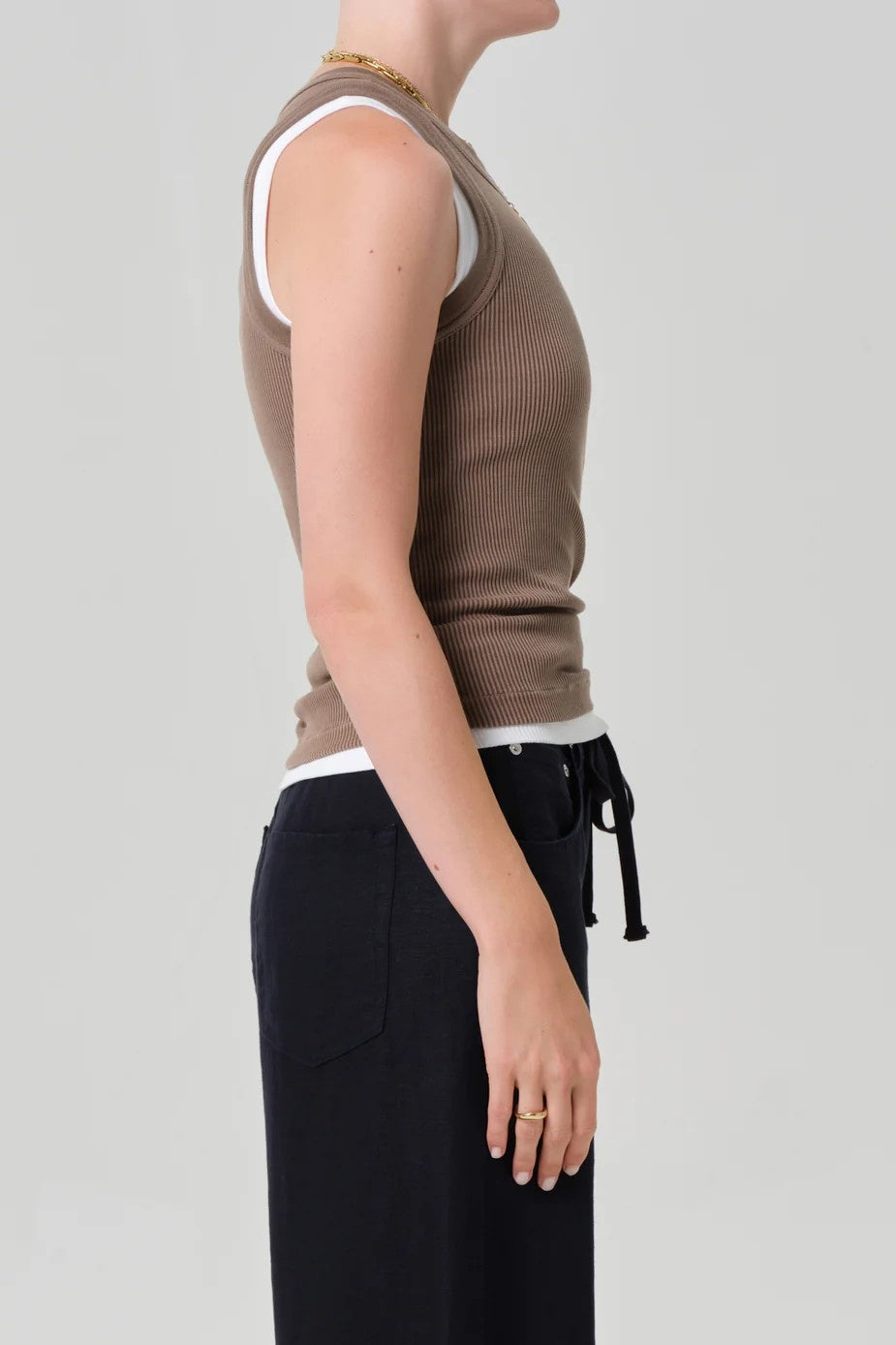 Person wearing a brown sleeveless top and black pants on a plain background