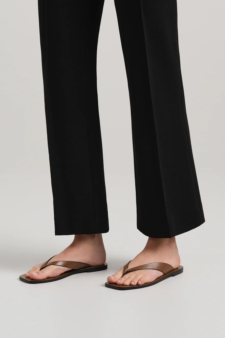 Person wearing black pants and brown sandals on a light gray background