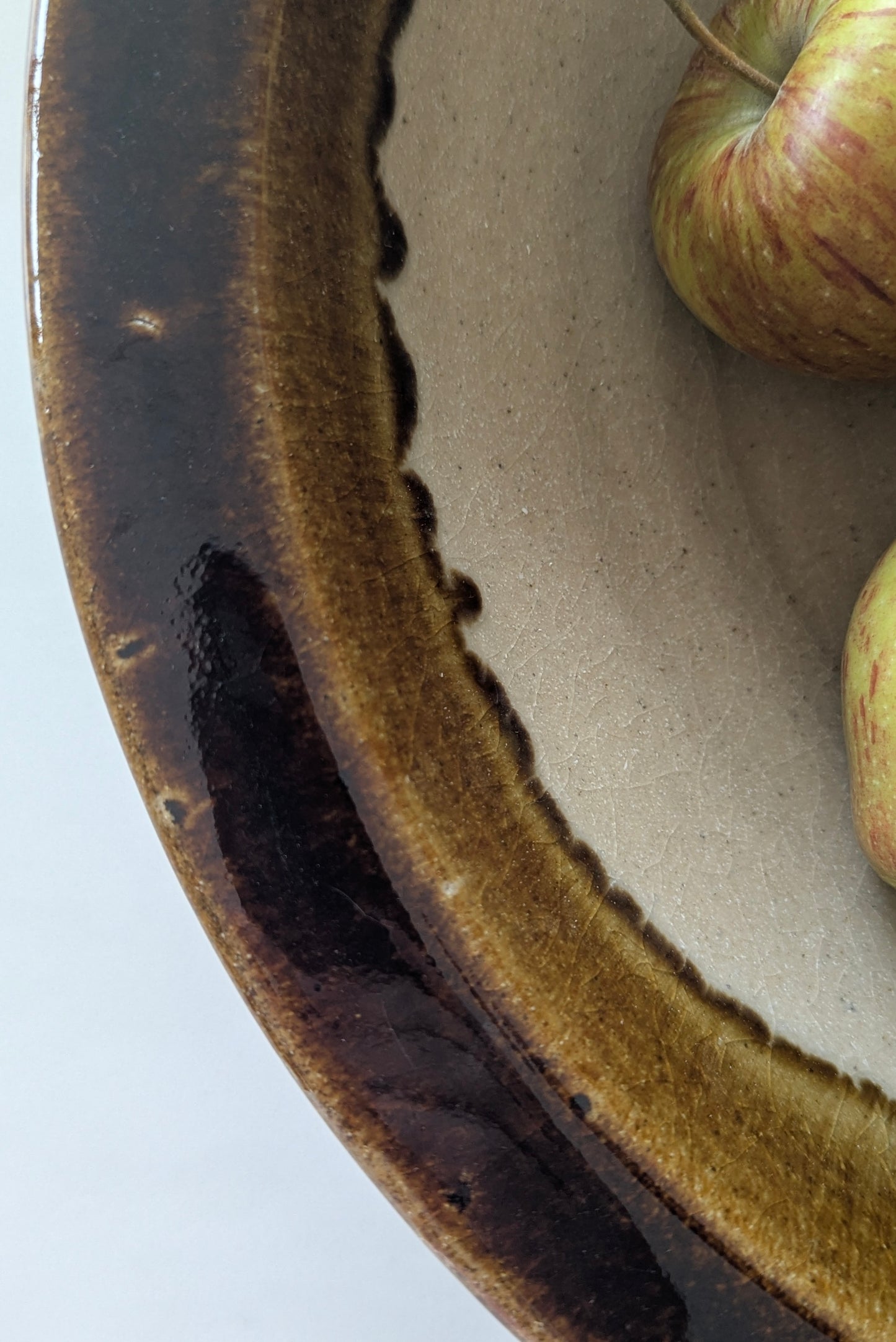 Close-up of a terracotta bowl with a dark brown rim and a light interior, containing two green apples.