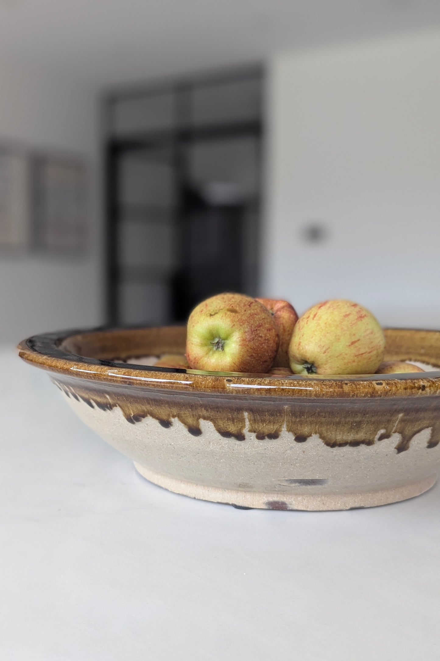 Terracotta bowl with apples on a white surface
