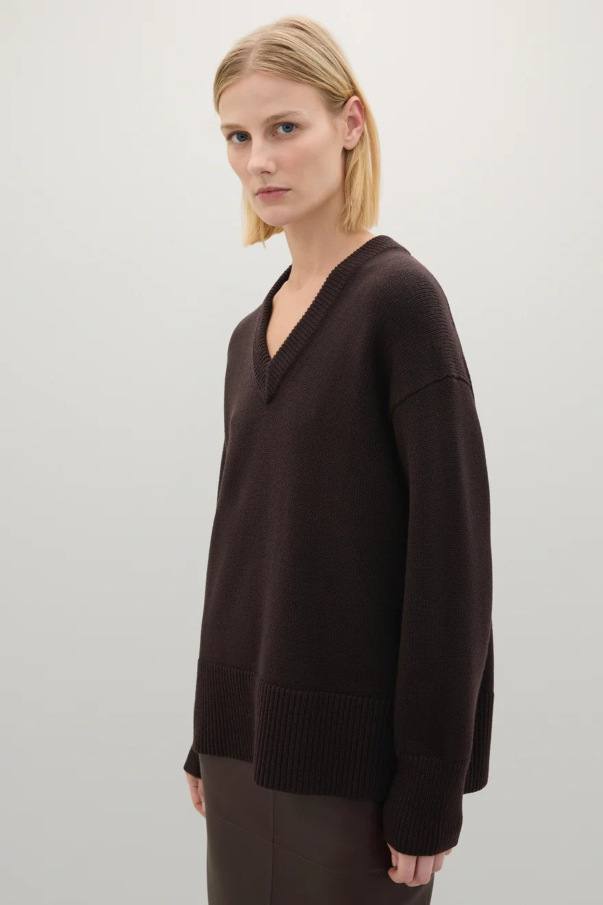 Woman wearing a dark brown sweater against a plain background