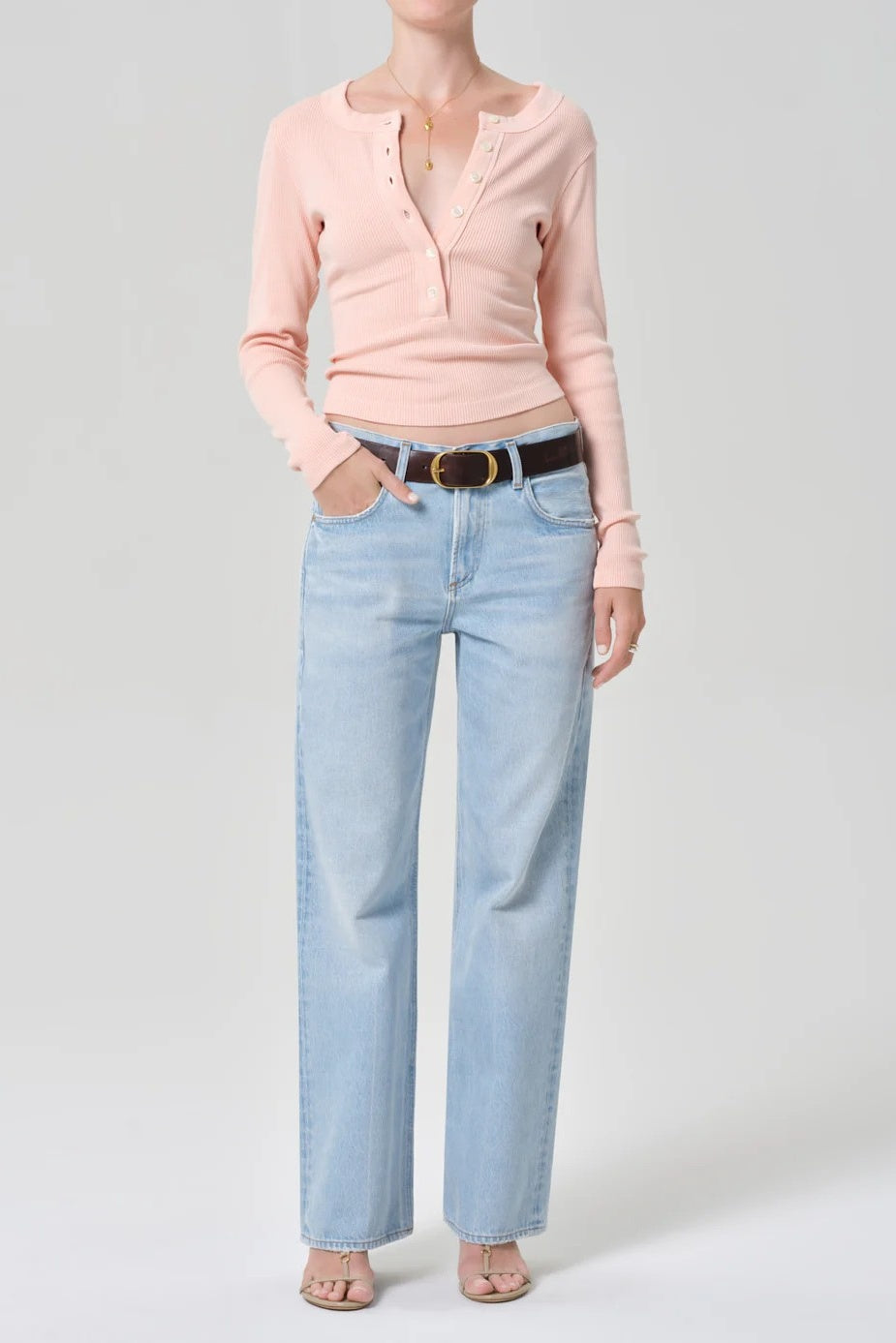 woman in peach top and pale jeans with her hand in her pocket 
